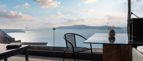 A balcony with a view of the sea, a glass table, a metal chair, and a wooden cabinet.