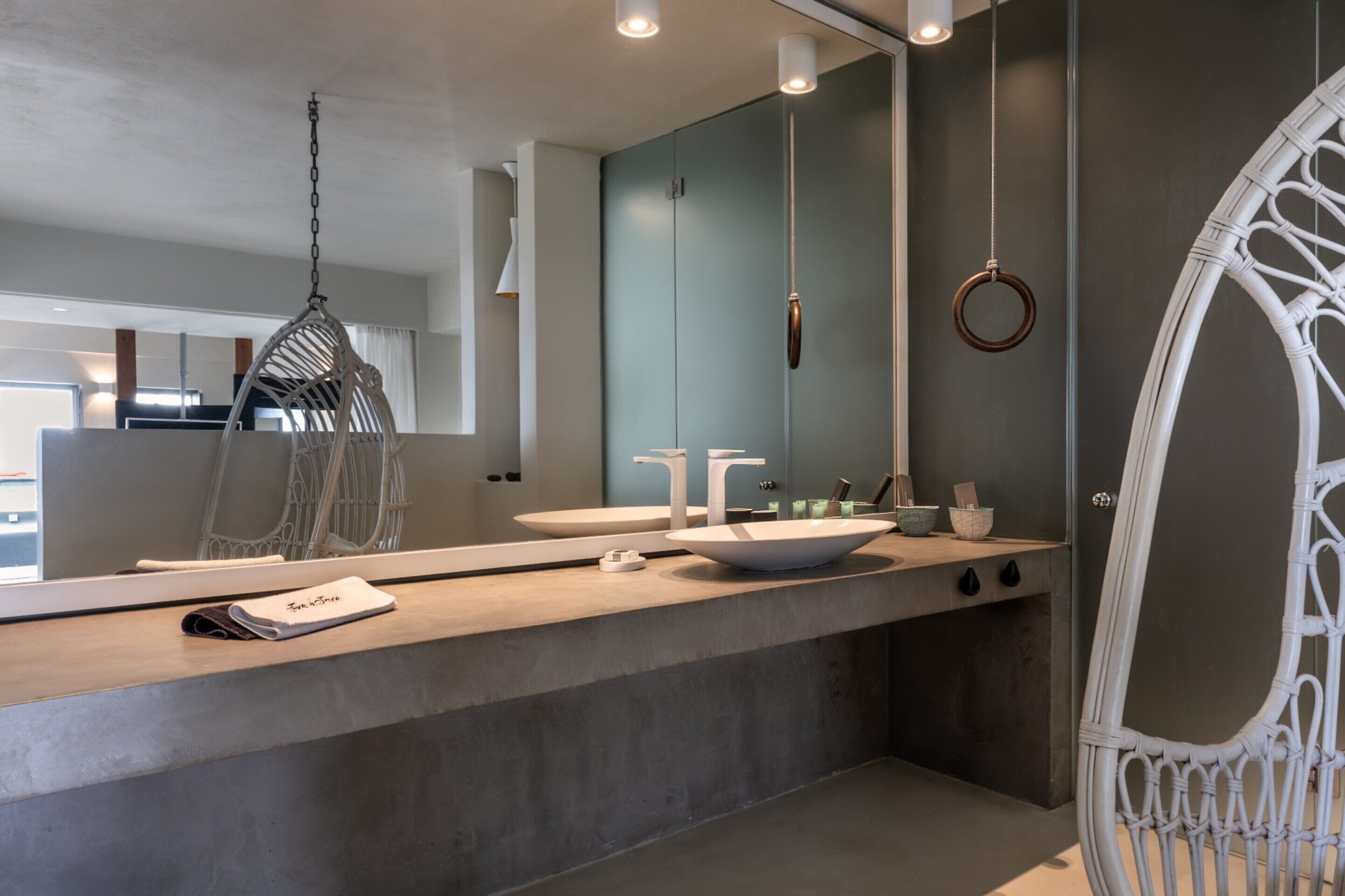 A modern bathroom with a large mirror, two sinks, a hanging chair, and a ring light.