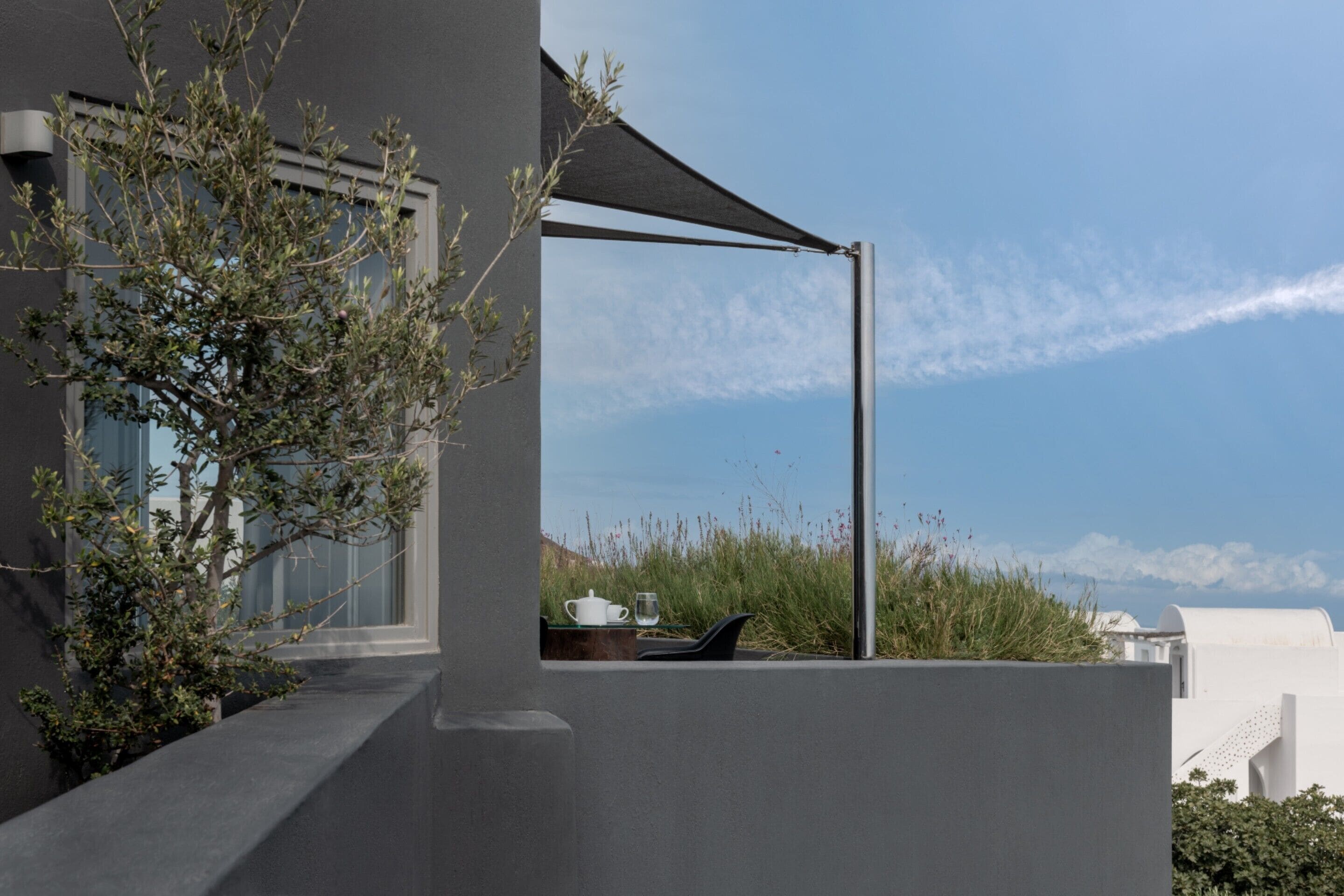 A modern building with a balcony, a table with a cup and glass, and a view of the sky and distant landscape.