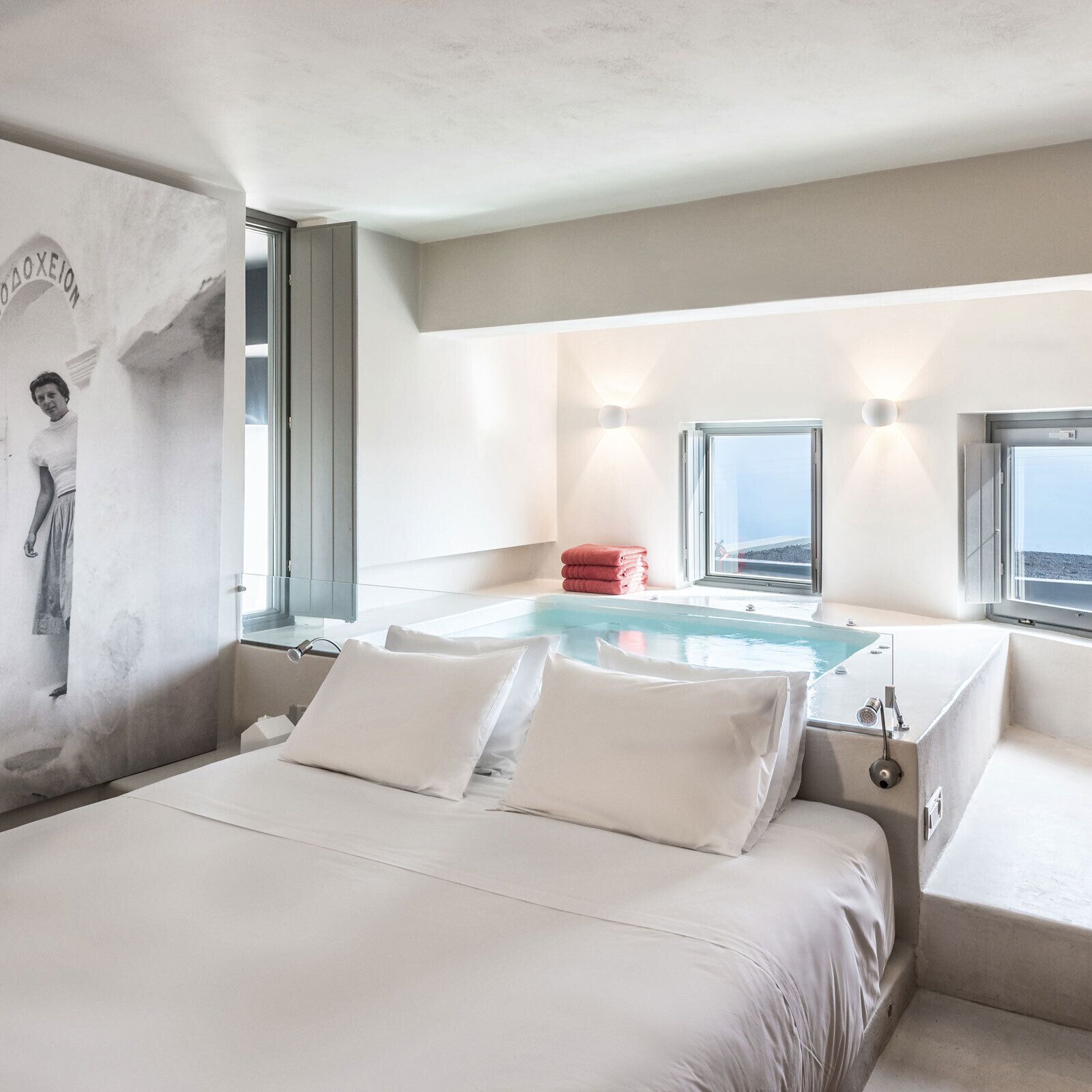 A modern hotel room with a large bed, a small sitting area, a built-in jacuzzi, and a view of the sea.