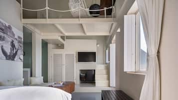 A modern hotel room with a loft bed, a flat-screen TV, a seating area with a table, and a large window.