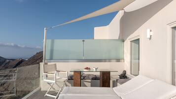 A balcony with a glass table, white lounge chairs, and a bed.