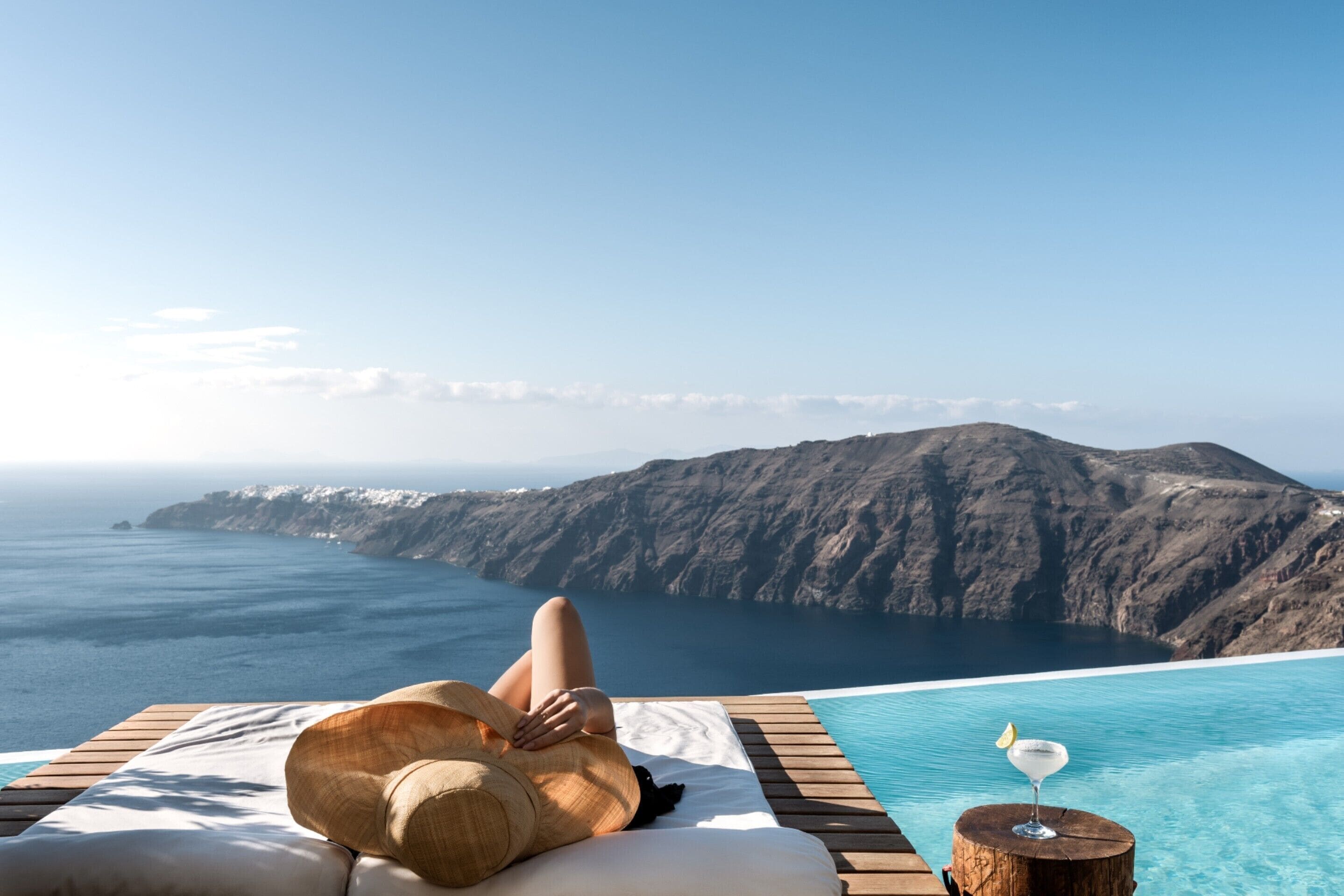 A person relaxing on a sun lounger with a view of the ocean and mountains.