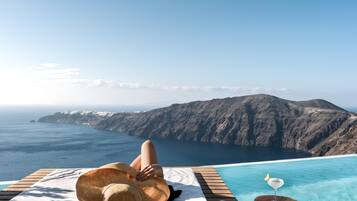 A person relaxing on a sun lounger with a view of the ocean and mountains.