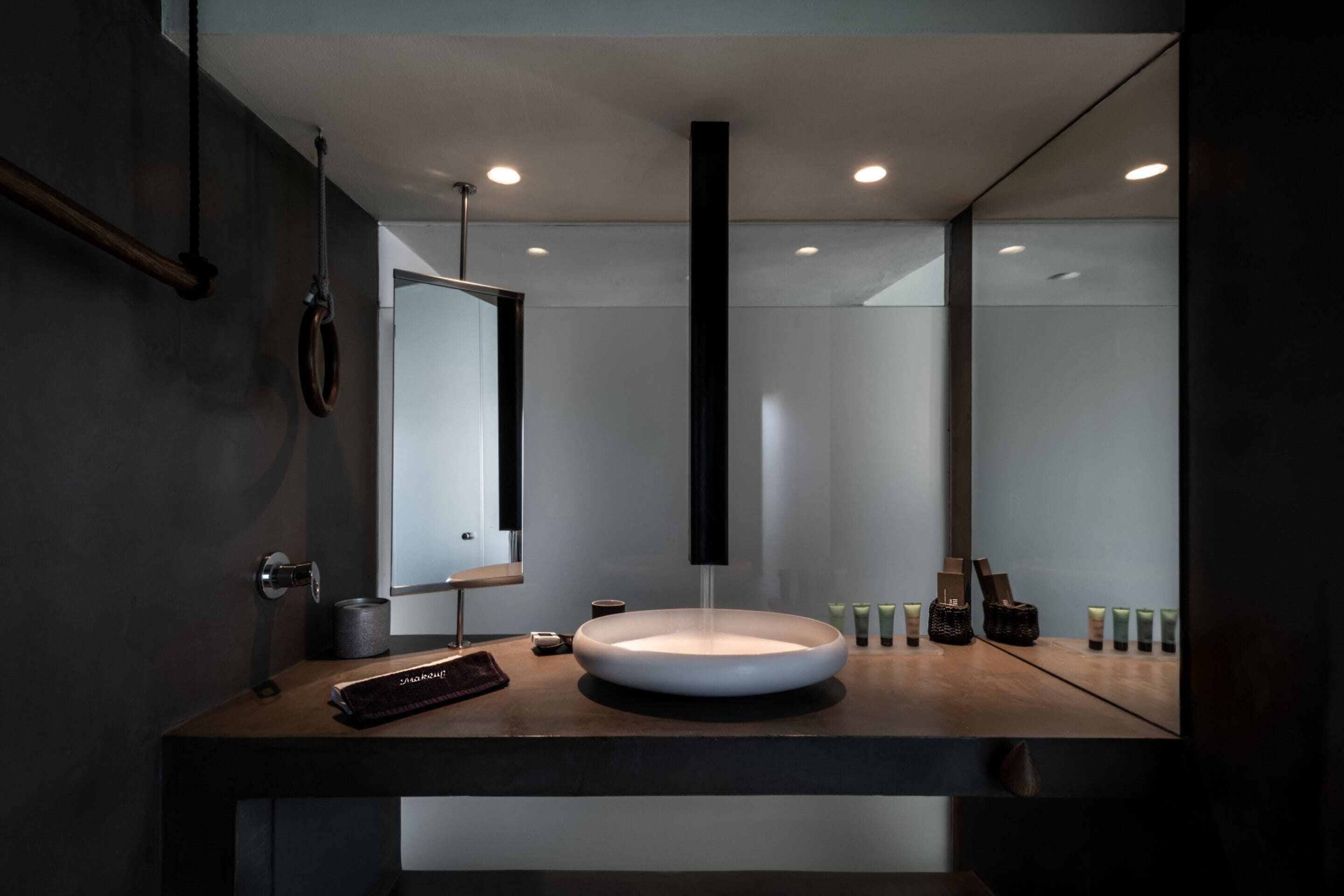 A modern bathroom with a round sink, a large mirror, and a vertical light fixture.