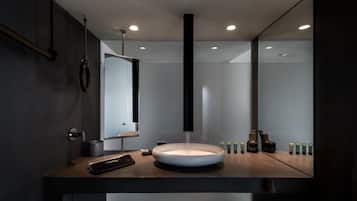 A modern bathroom with a round sink, a large mirror, and a vertical light fixture.