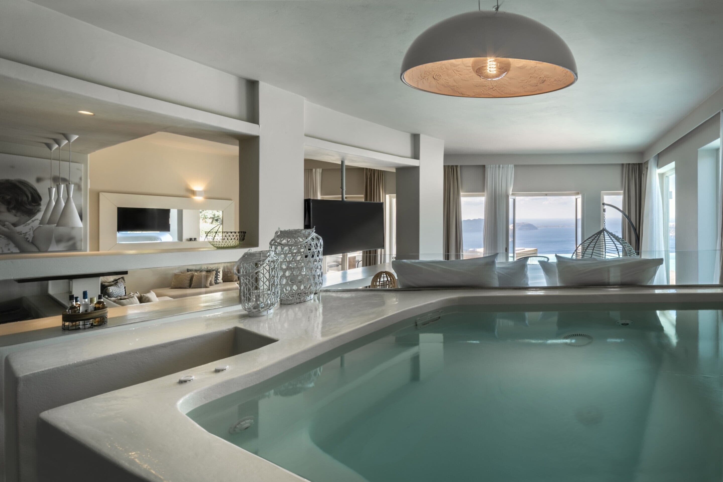 A modern indoor swimming pool with a large mirror, a television, and a unique ceiling light fixture.