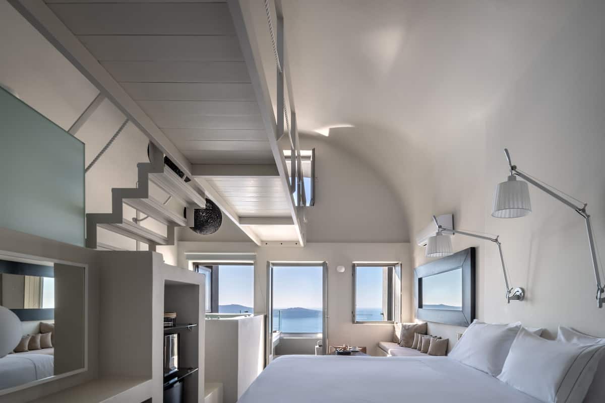 A modern hotel room with a large bed, a desk, a chair, and a view of the sea.