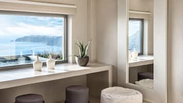 A modern bathroom with a large mirror, a bathtub, and a window overlooking a body of water.