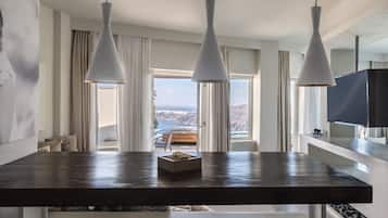 A dining area with a dark wooden table, three white pendant lights, and a view of the sea through large windows.
