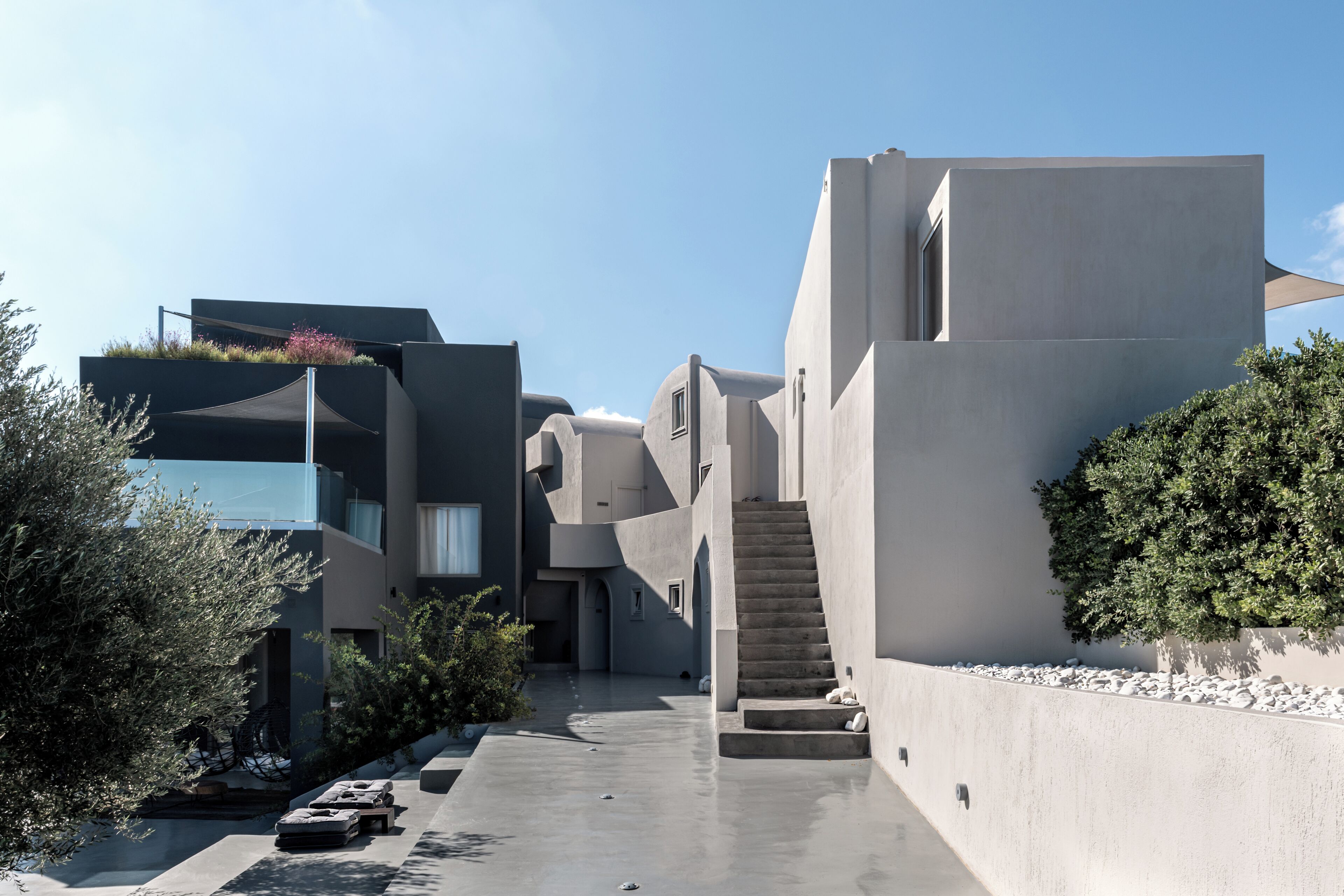 A modern architectural building with a concrete facade, a central staircase, and a small garden area.