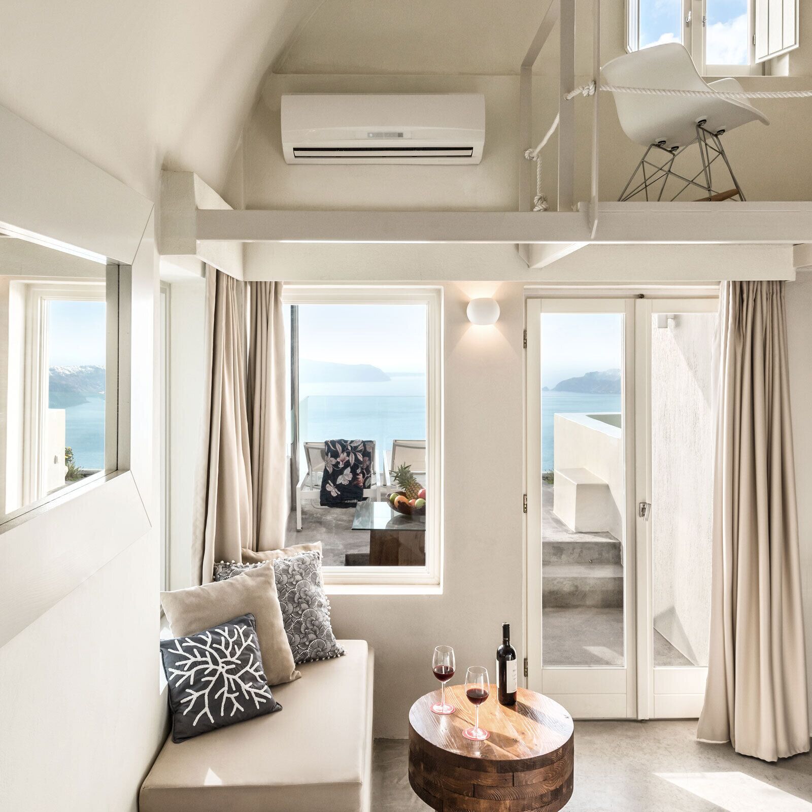 A modern living room with a sofa, a round wooden coffee table, and a view of the sea through large windows.