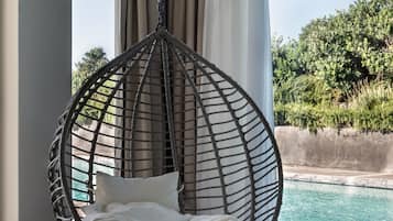 A hanging chair with cushions by a window overlooking a pool.