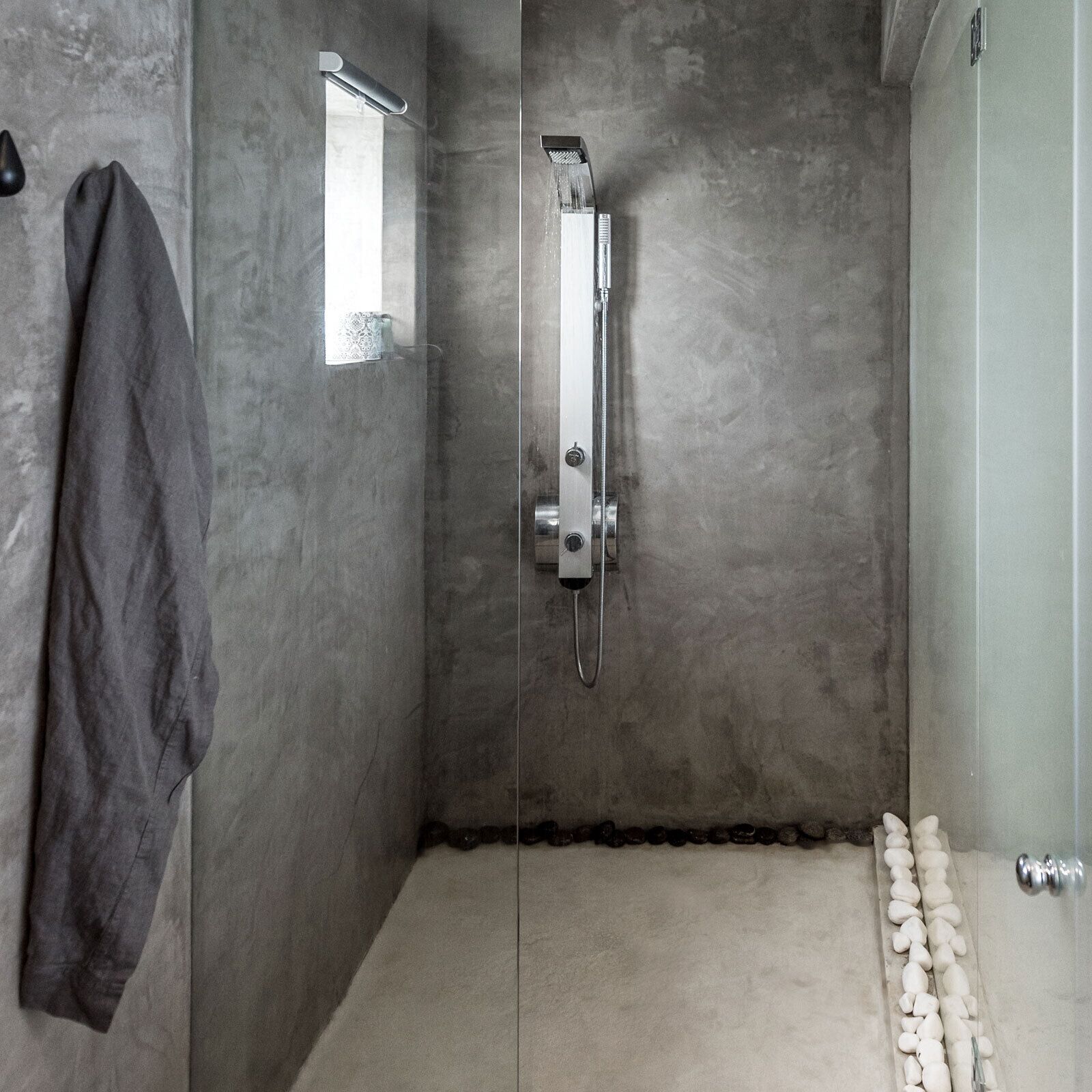 A modern shower with a handheld showerhead, a towel rack, and a small window.