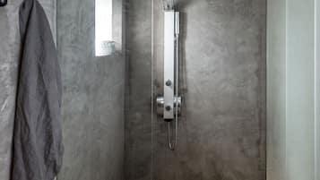 Une douche moderne équipée d’un pommeau de douche à main, d’un porte-serviettes et d’une petite fenêtre.
