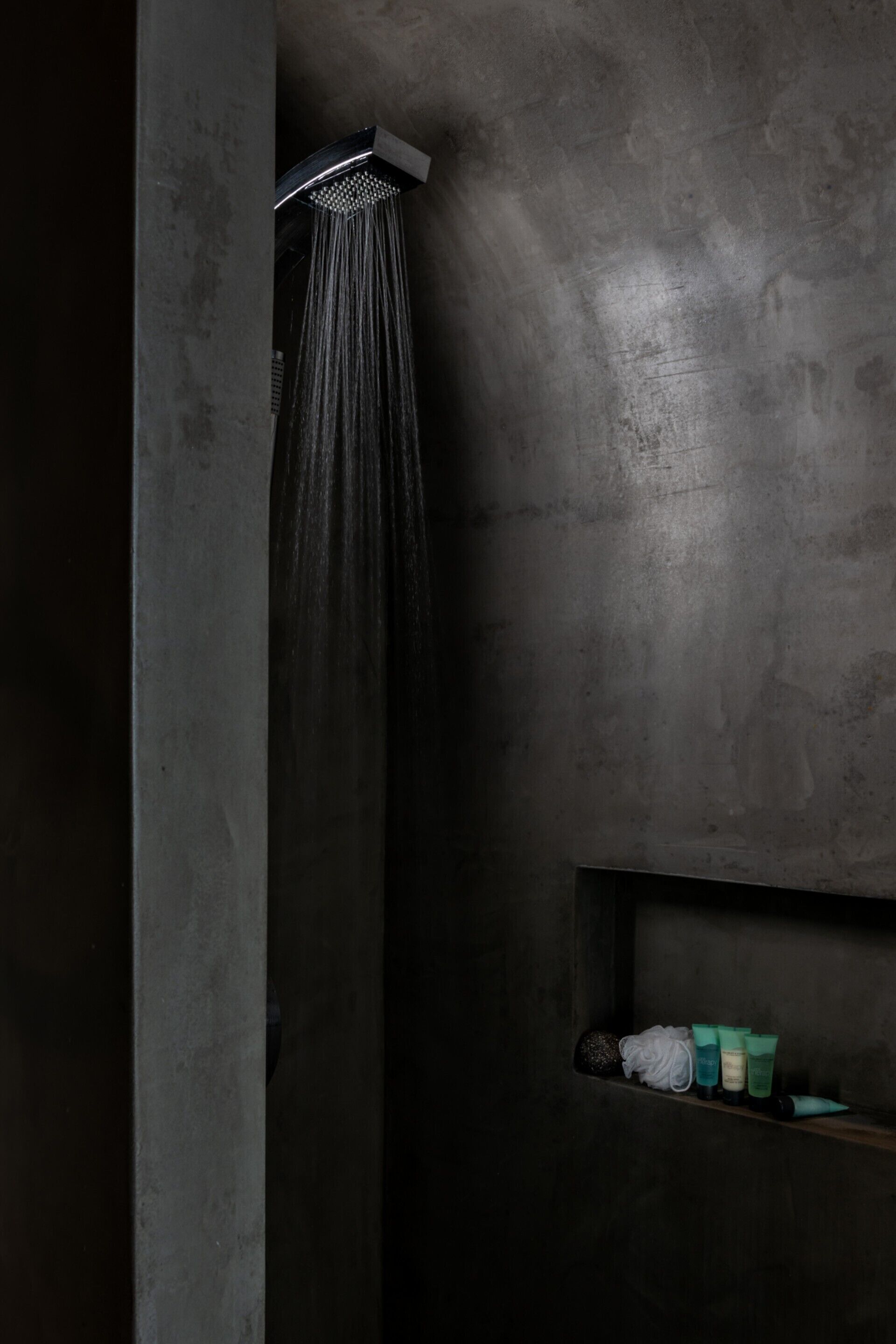 Eine Dusche mit modernem Design, ein Ablagefach mit Pflegeprodukten und eine strukturierte Wand.