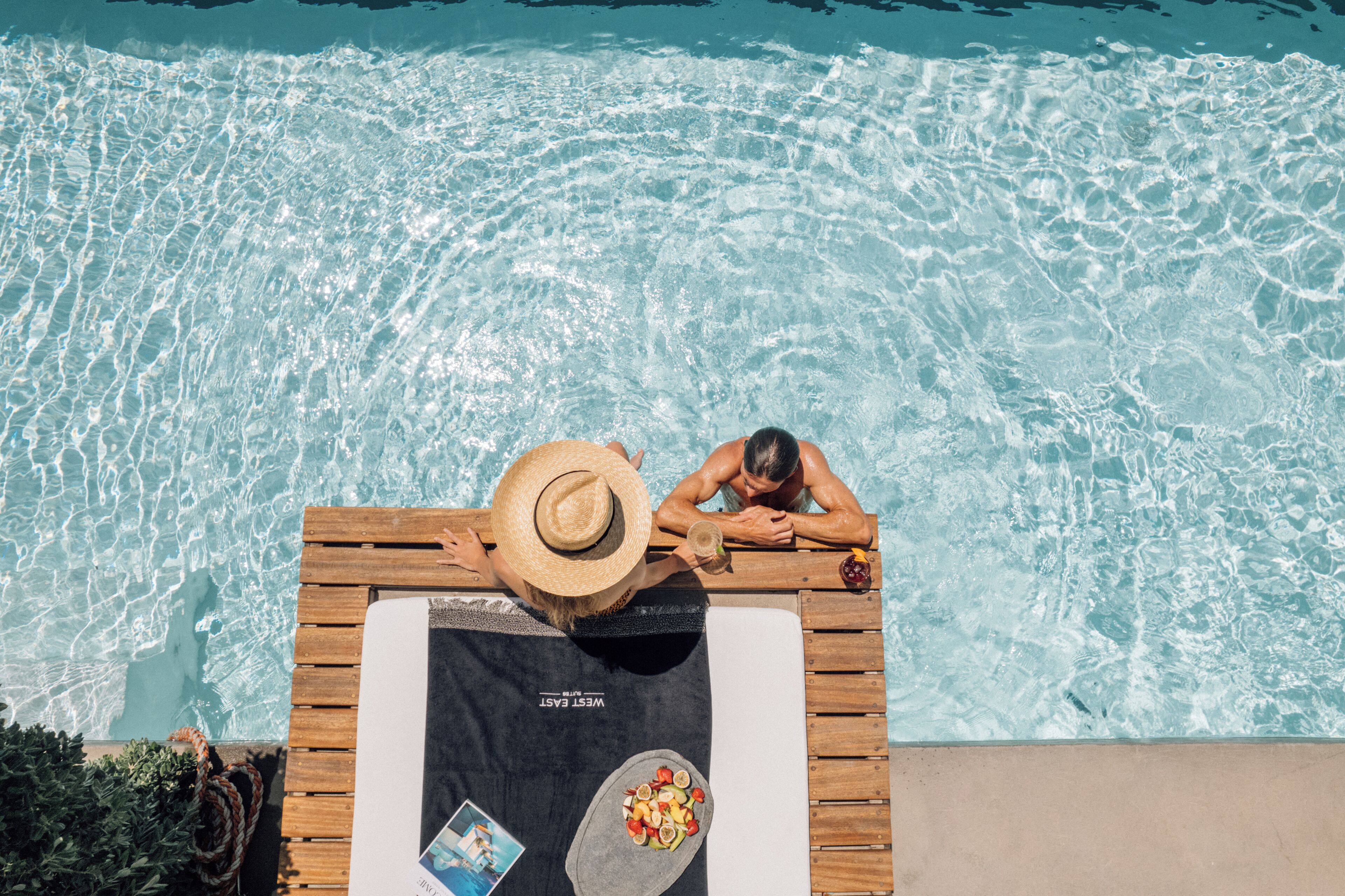 Zona de piscina con terraza de madera, sillas de descanso y una toalla con un cuenco de frutas.