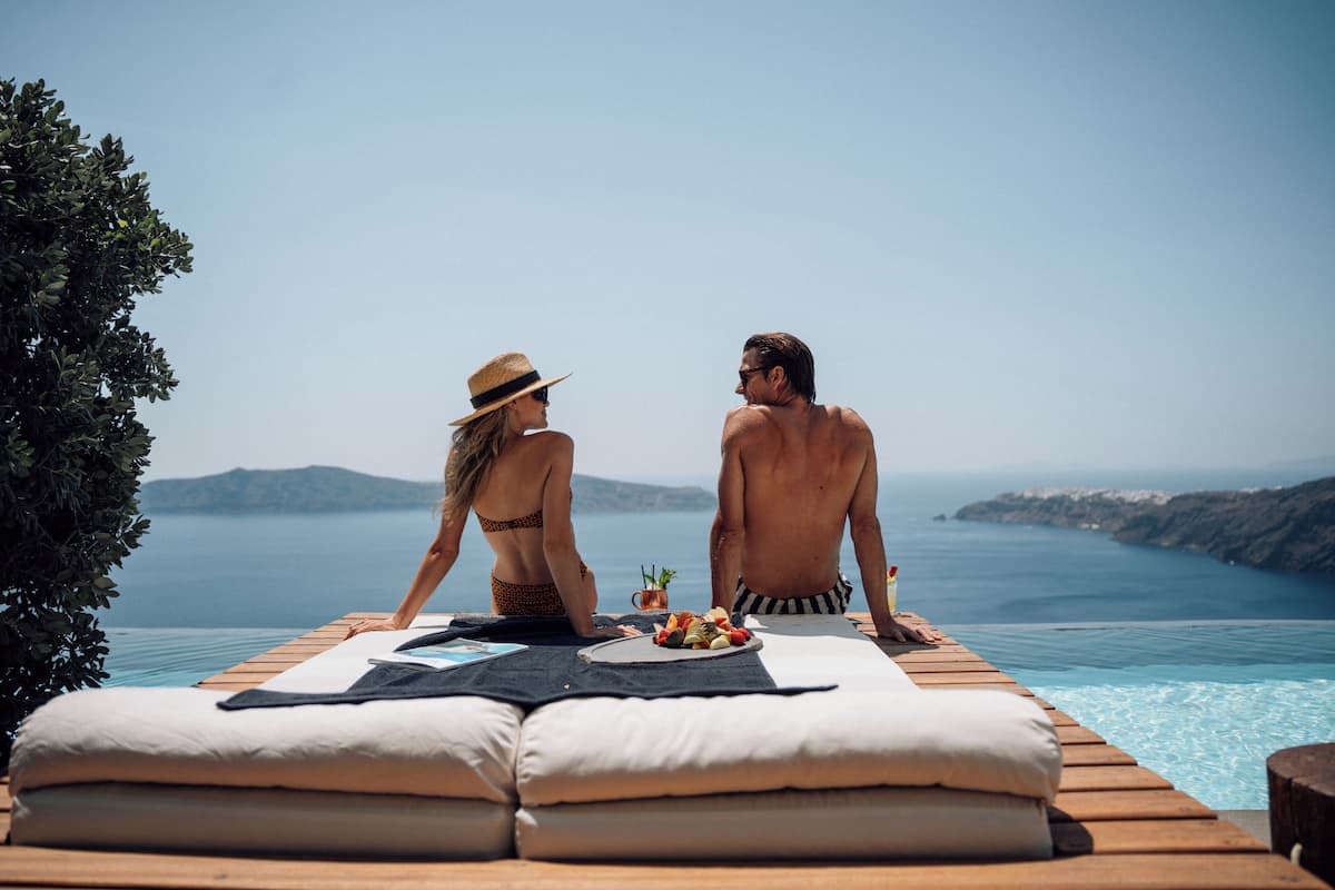 A couple relaxing on a wooden deck overlooking a body of water with mountains in the distance.