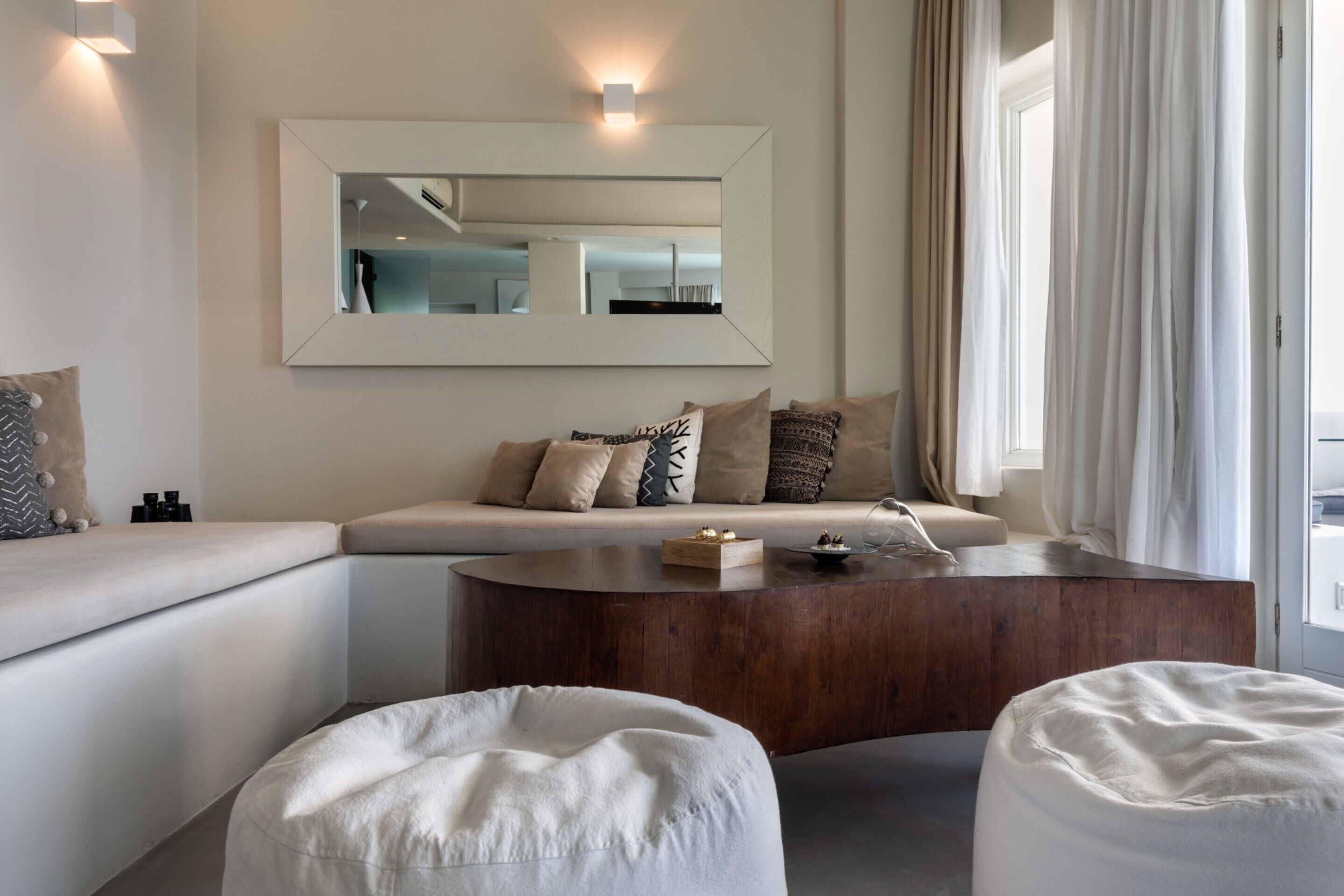 A modern living room with a sofa, ottomans, a wooden coffee table, and a large mirror on the wall.