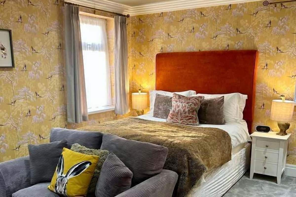 Une chambre à coucher avec un lit, une table de chevet, une chaise et une fenêtre avec des rideaux.