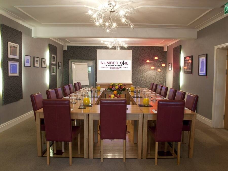 Une salle de conférence avec une longue table, des chaises rouges et un lustre. Une pancarte indique : « NUMBER ONE SOUTH BEACH ».