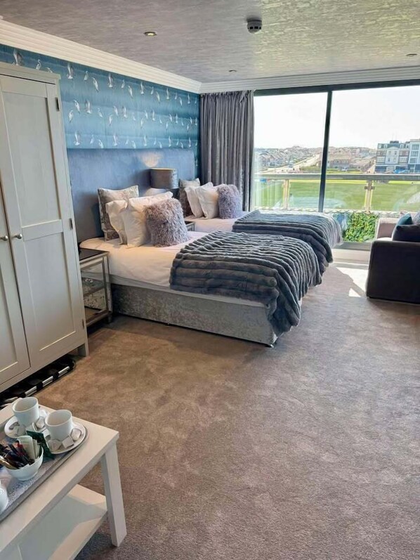 Quarto de hotel com uma cama grande, uma escrivaninha com xícara e pires, e vista para o exterior.