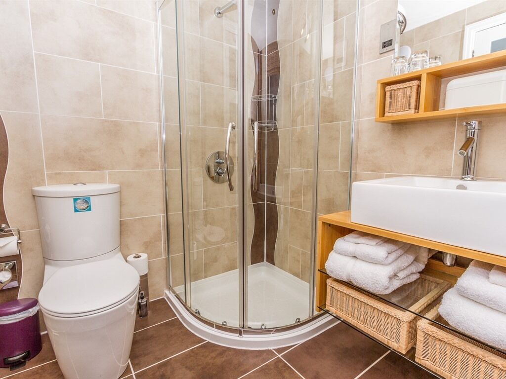 Une salle de bain avec une douche à parois de verre, un lavabo blanc et une étagère en bois où sont posées des serviettes.