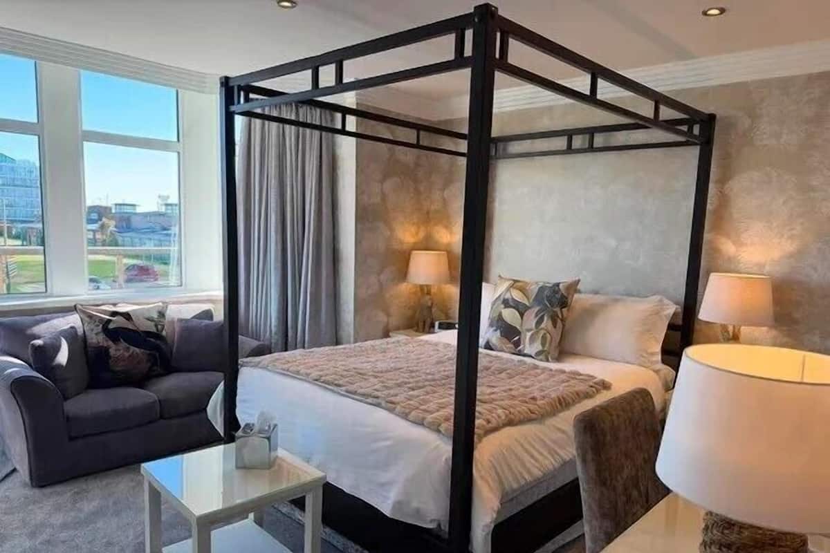 Un lit à baldaquin avec vue sur la ville, un canapé gris et une petite table avec une lampe.