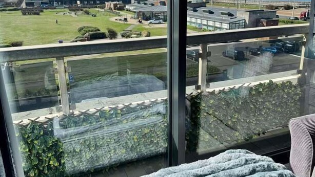 Ein Balkon mit Blick auf eine Küstenlandschaft, darunter Gebäude und ein Parkplatz.