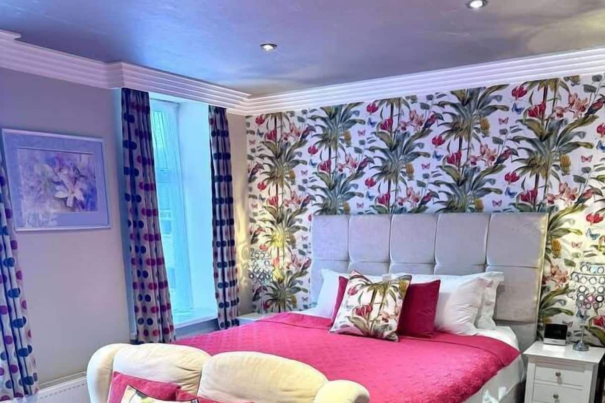 Une chambre à coucher comprenant un lit, un canapé, une table de chevet et un mur recouvert d’un papier peint à motifs floraux.