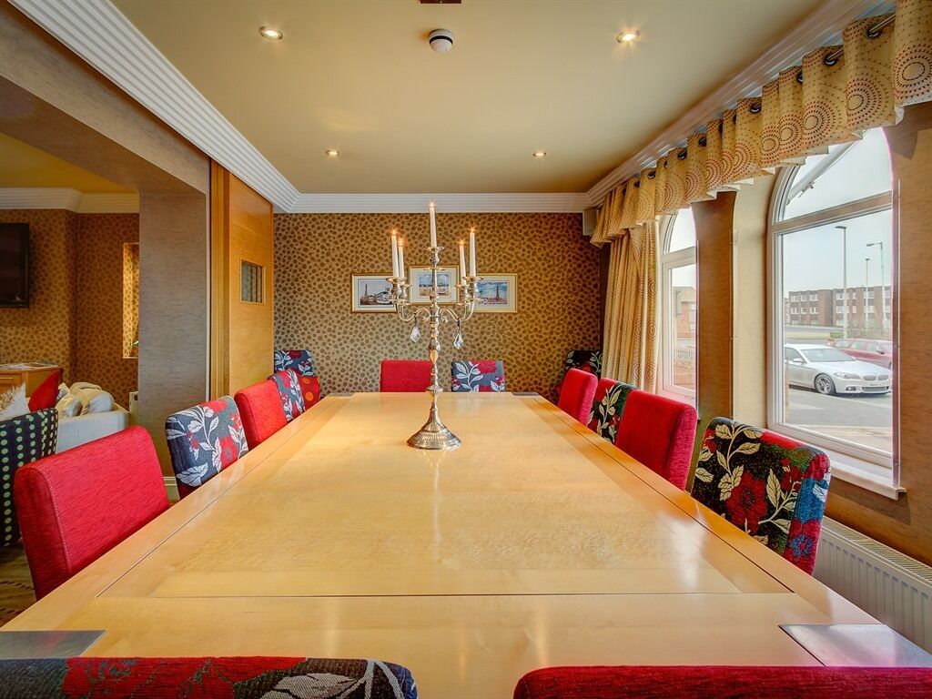 A conference room with a long table, red upholstered chairs, a candelabra, and a view of the street through large windows.