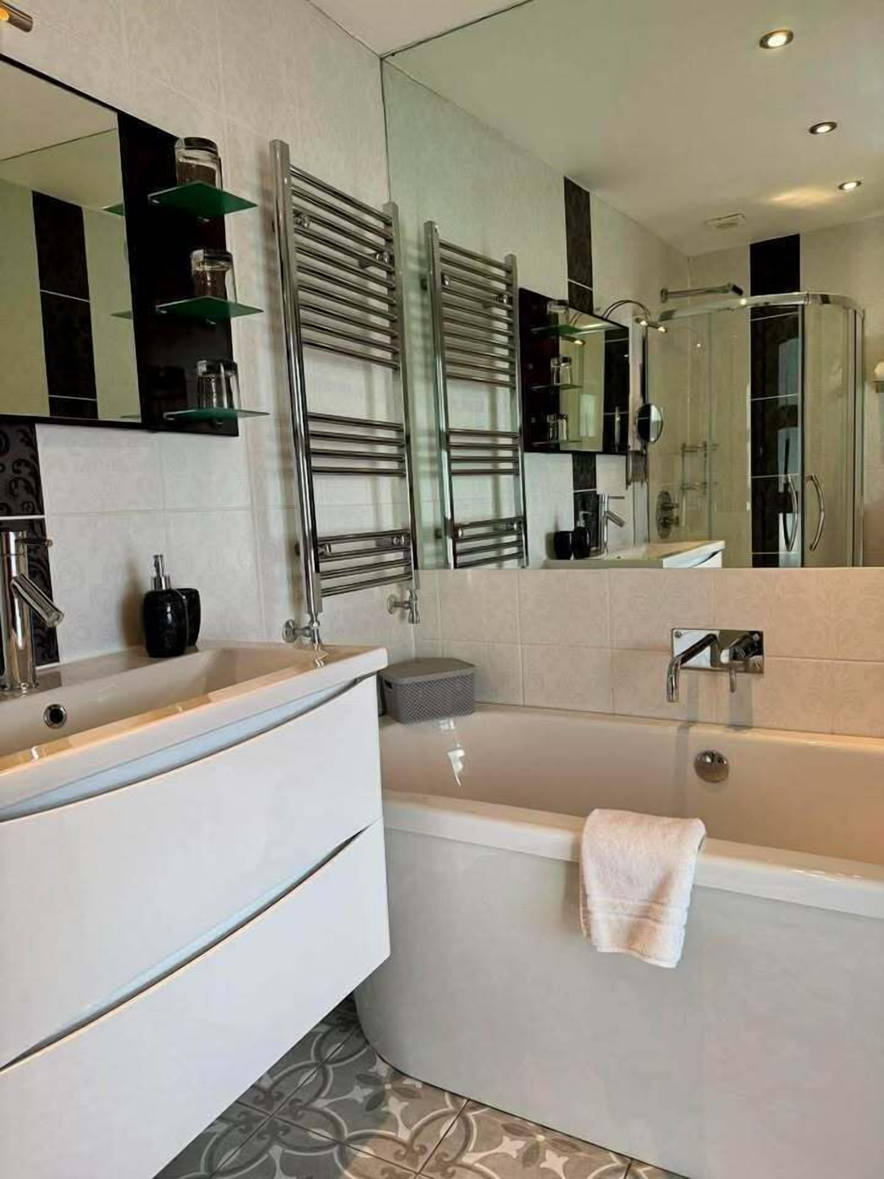 A modern bathroom with a large mirror, a bathtub, a vanity with a sink, and a towel rack.