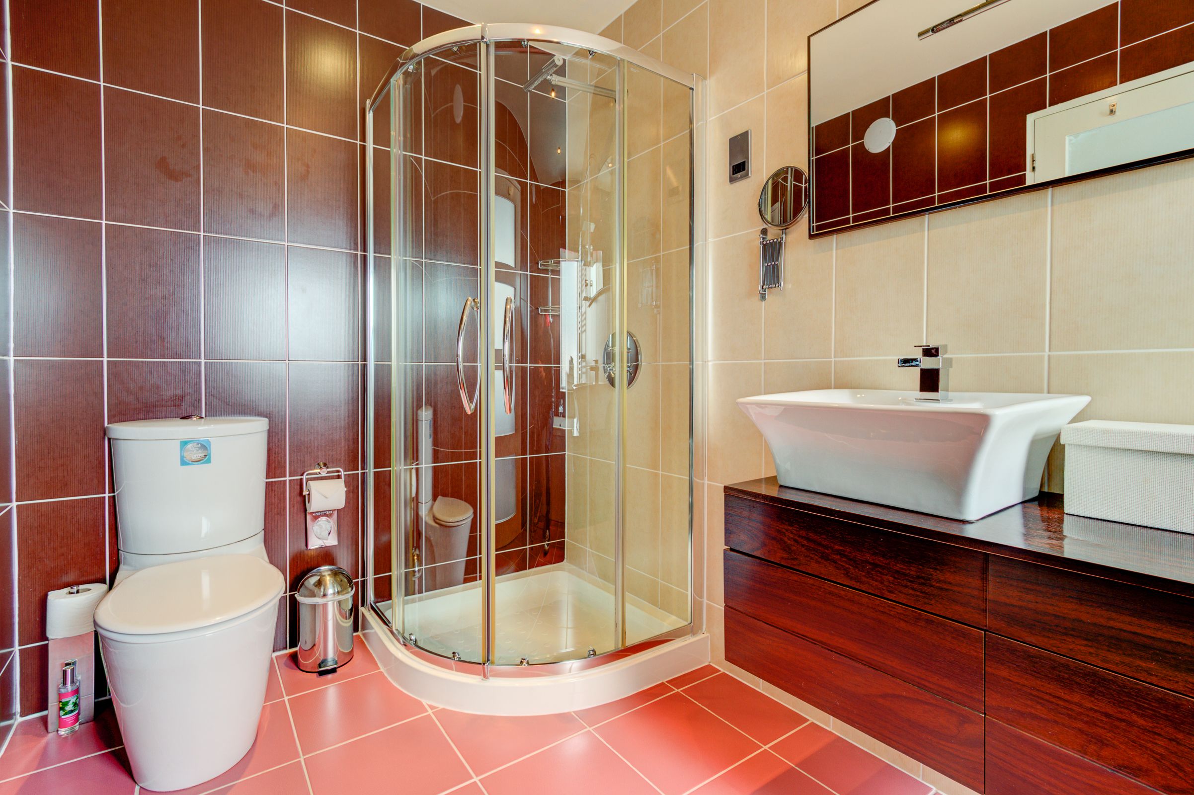 Un baño moderno con cabina de ducha de vidrio, un lavabo blanco y un mueble de tocador de madera.