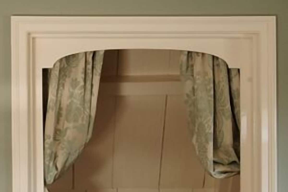A room with a built-in wardrobe, a bed with a patterned bedspread, and a small window with curtains.