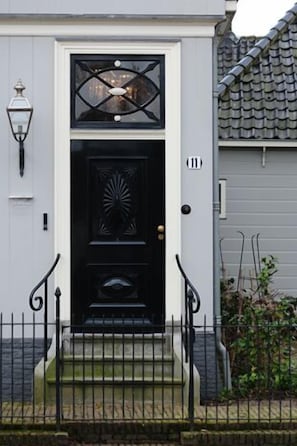 Una puerta principal negra con un panel de vidrio decorativo, un pequeño porche con escalones y una cerca de metal negra.
