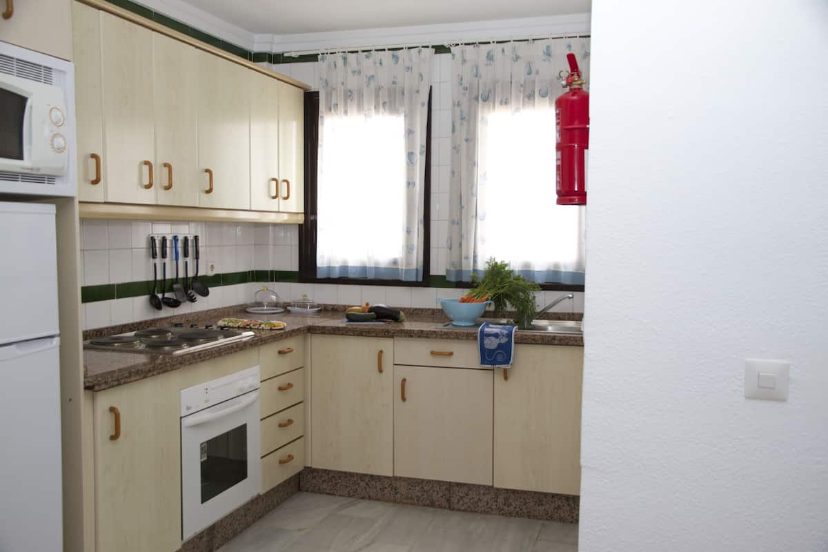 Een keuken met houten kastjes, een magnetron, een fornuis en een spoelbak.