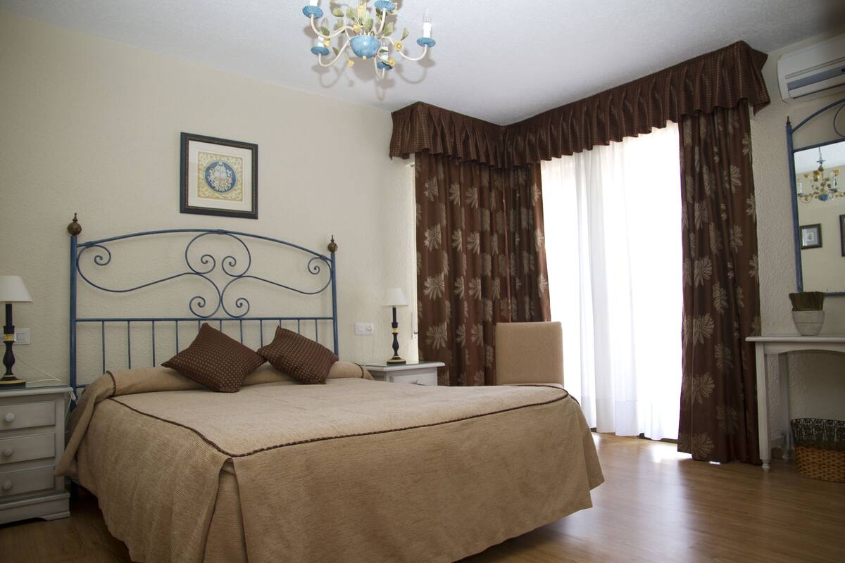 Een slaapkamer met een groot bed, een nachtkastje, een stoel, een kroonluchter en een open haard.