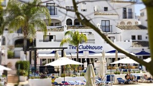 Un hotel llamado 'The Clubhouse' con piscina, sillones de descanso, sombrillas y palmeras.