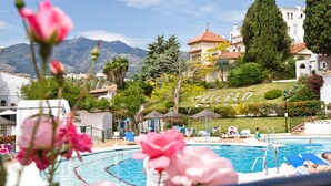 Zona de piscina con sillones de descanso, vista despejada de montañas y un edificio con la palabra "PUERTO" escrita.