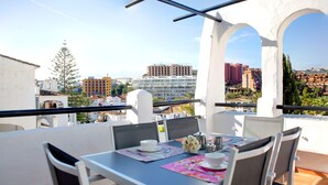 Un balcón con una mesa preparada para dos personas, con vistas a un paisaje urbano y varios edificios.