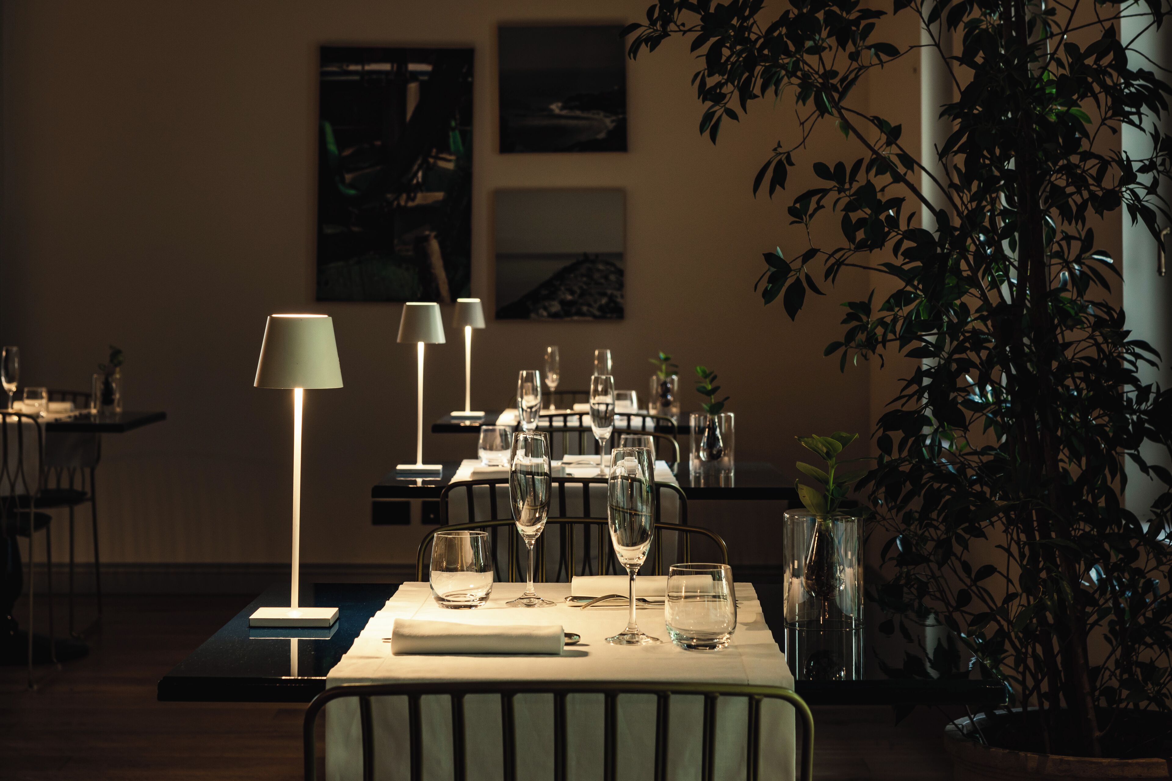 Un restaurant à la lumière tamisée, avec une table dressée pour le dîner, agrémentée de plusieurs verres à vin et d’une lampe.
