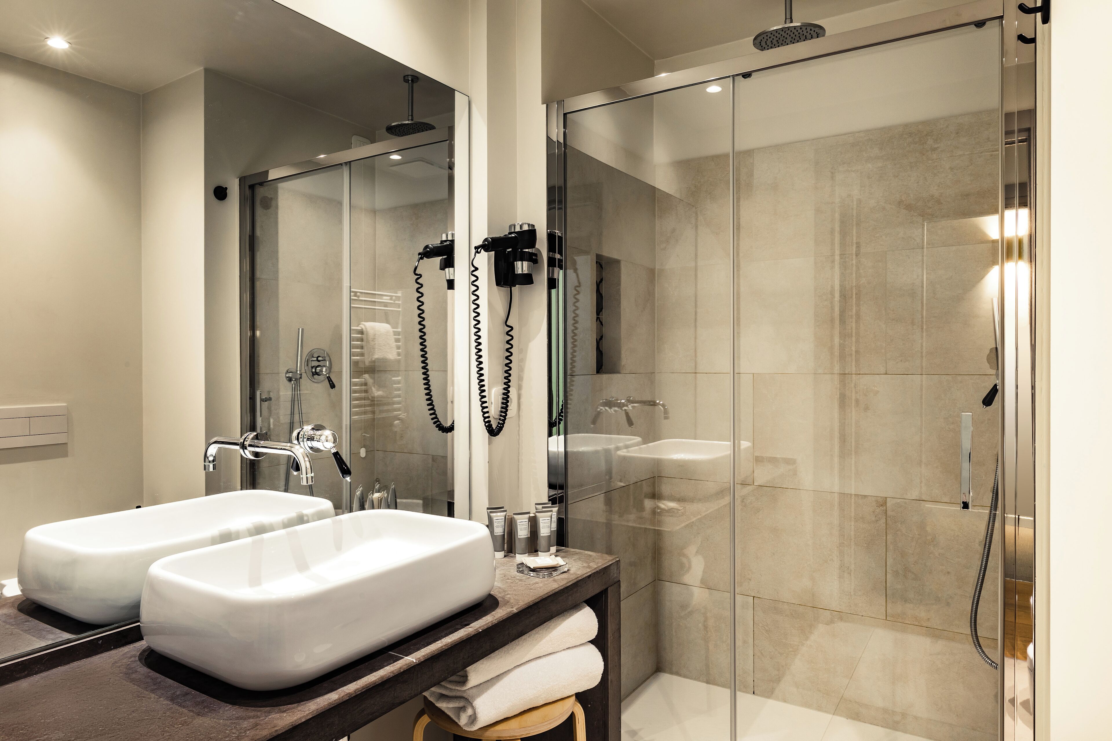 A modern bathroom with two sinks, a glass shower enclosure, and a vanity with a mirror.