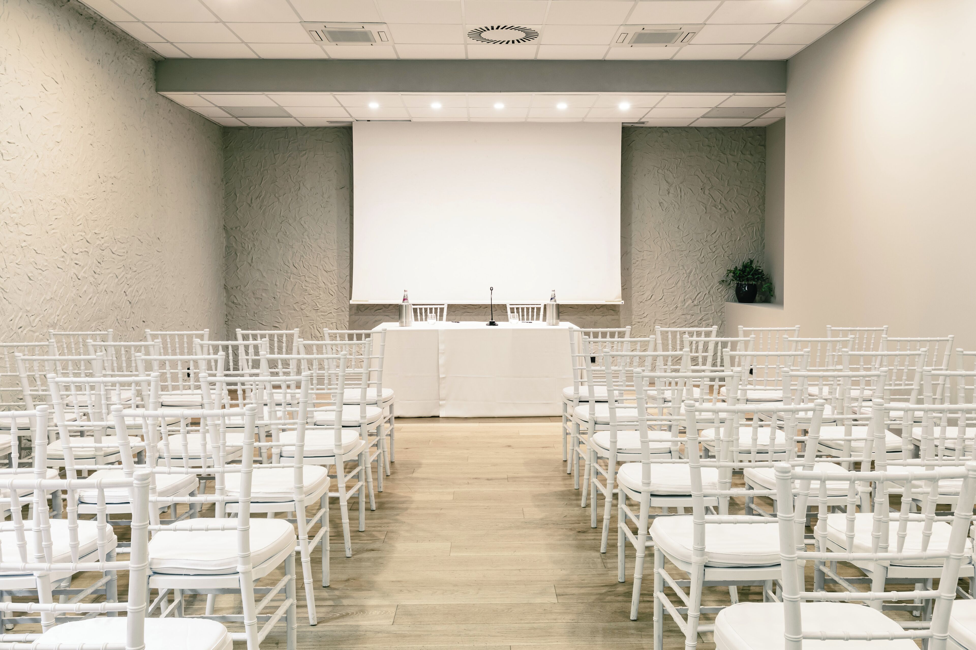 A conference room with rows of white chairs and a large screen at the front.