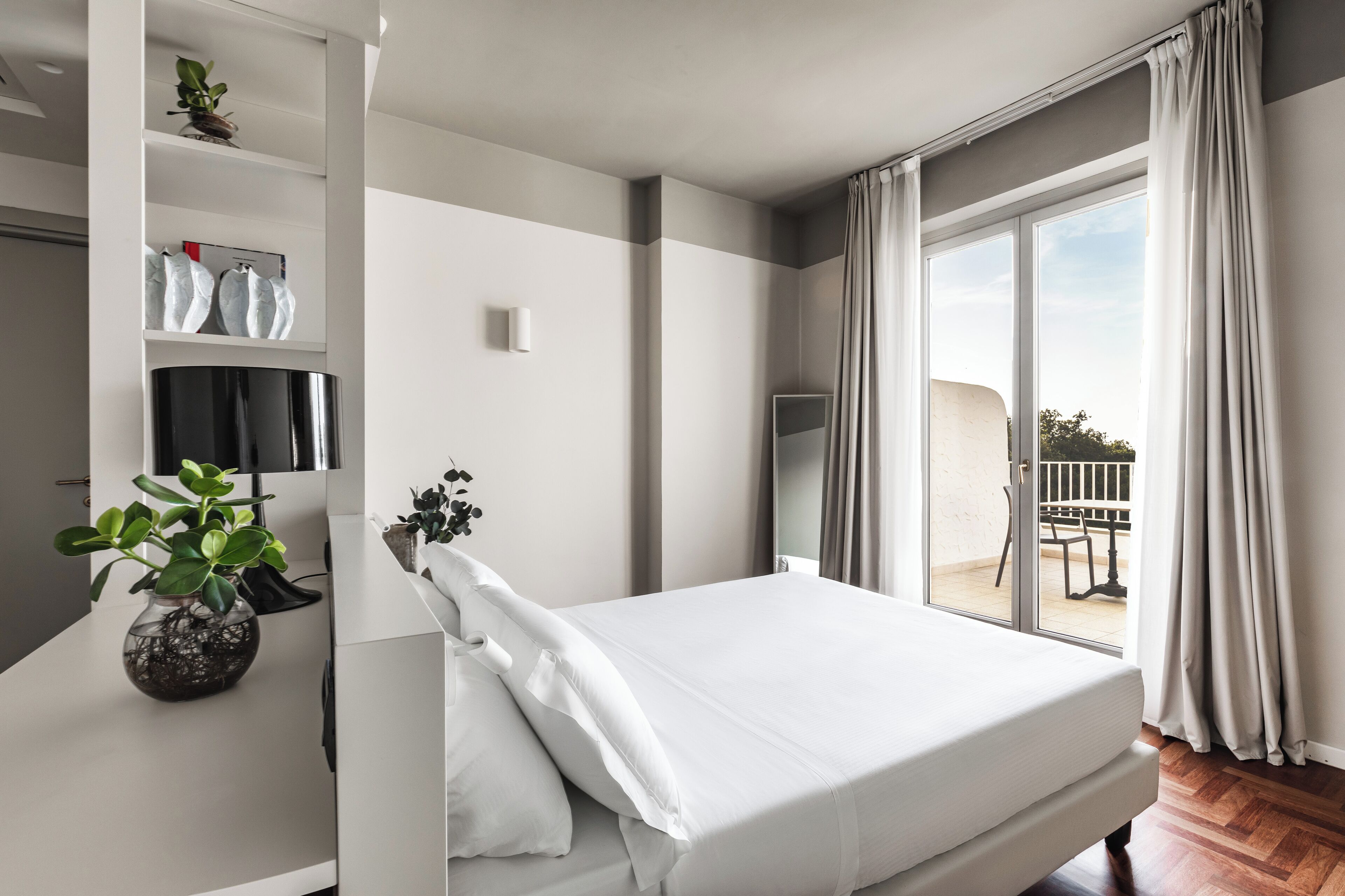 Une chambre moderne avec un grand lit, une télévision, une plante et un balcon avec vue.