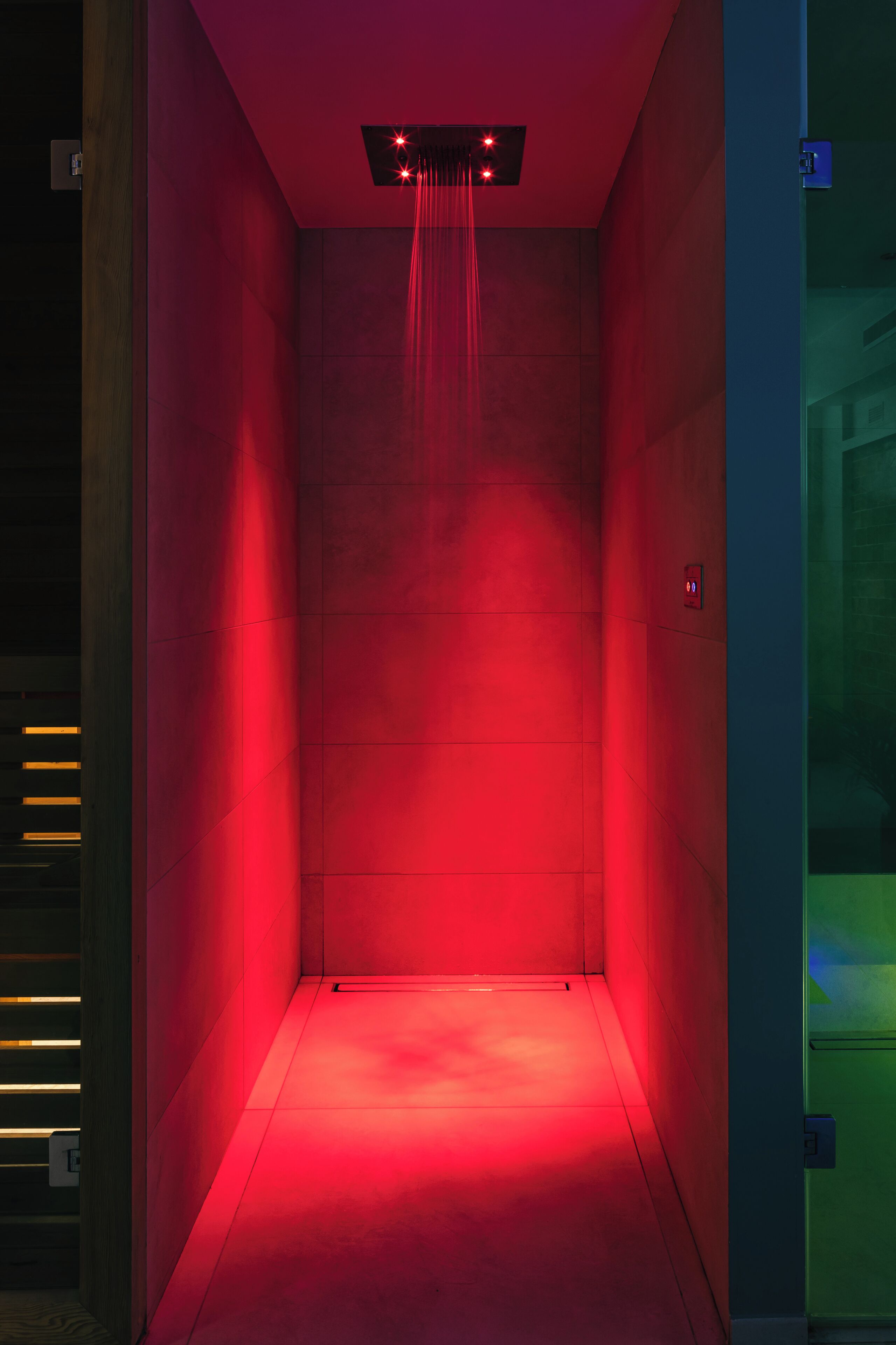 Un ascensor iluminado en rojo con un diseño moderno, que incluye un panel de control en la pared y una señal de salida de emergencia visible.