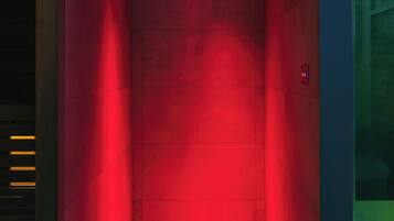 Un ascensor iluminado en rojo con un diseño moderno, que incluye un panel de control en la pared y una señal de salida de emergencia visible.