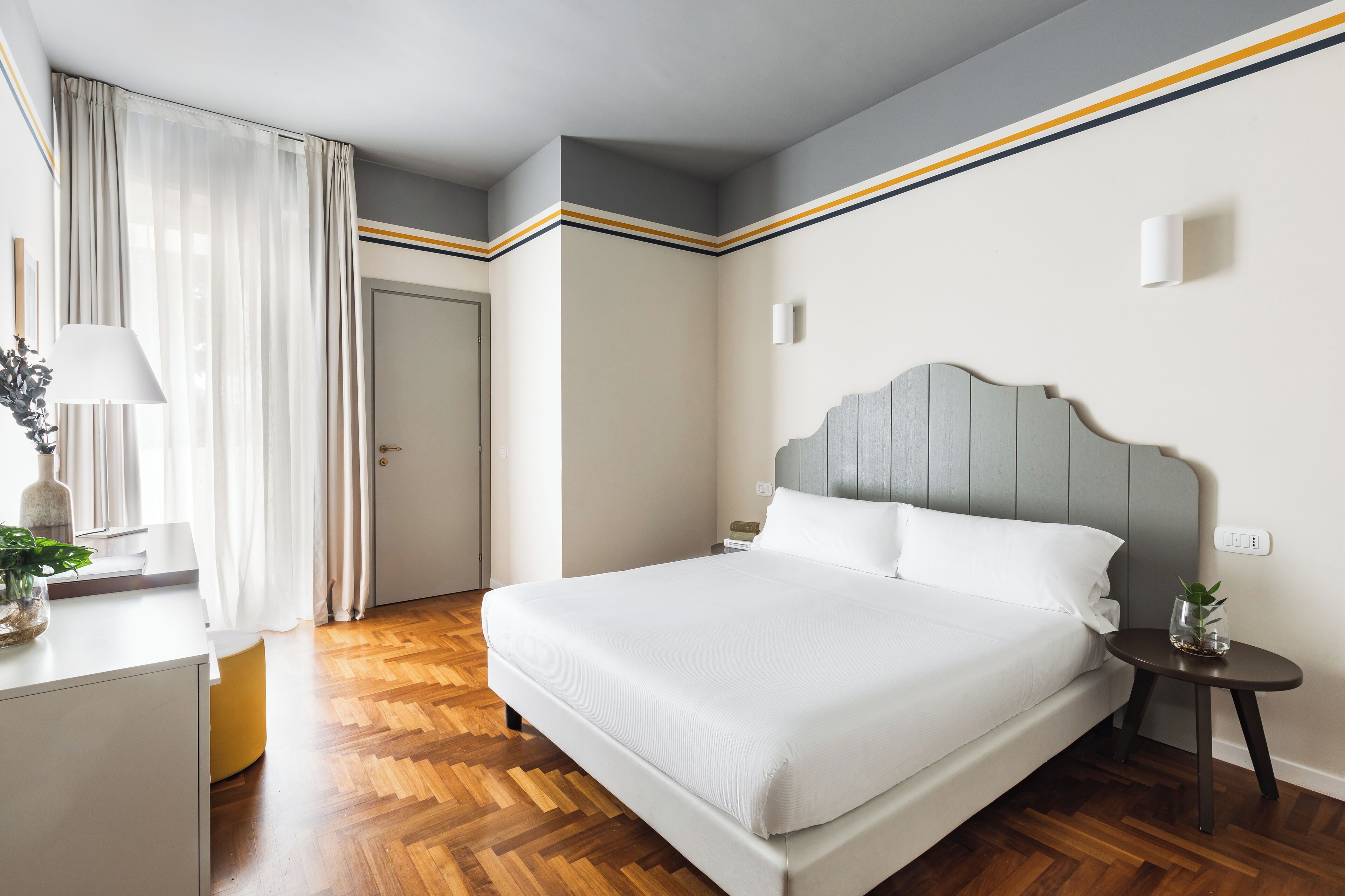 Ein ordentlich eingerichtetes Schlafzimmer mit Bett, Nachttisch, Lampe und einer Topfpflanze.