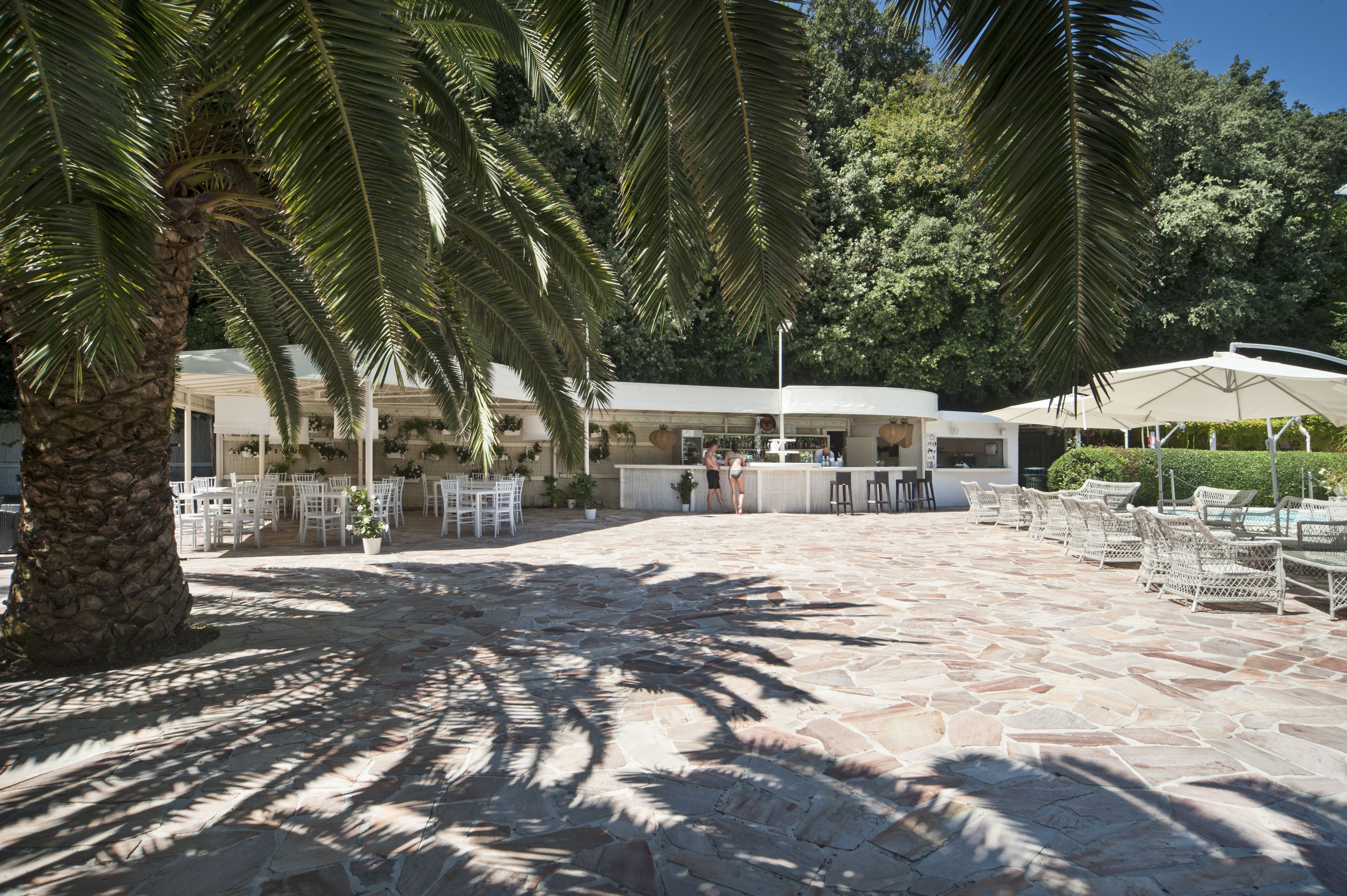 Un patio exterior con suelo de piedra, mobiliario de mimbre blanco y palmeras.