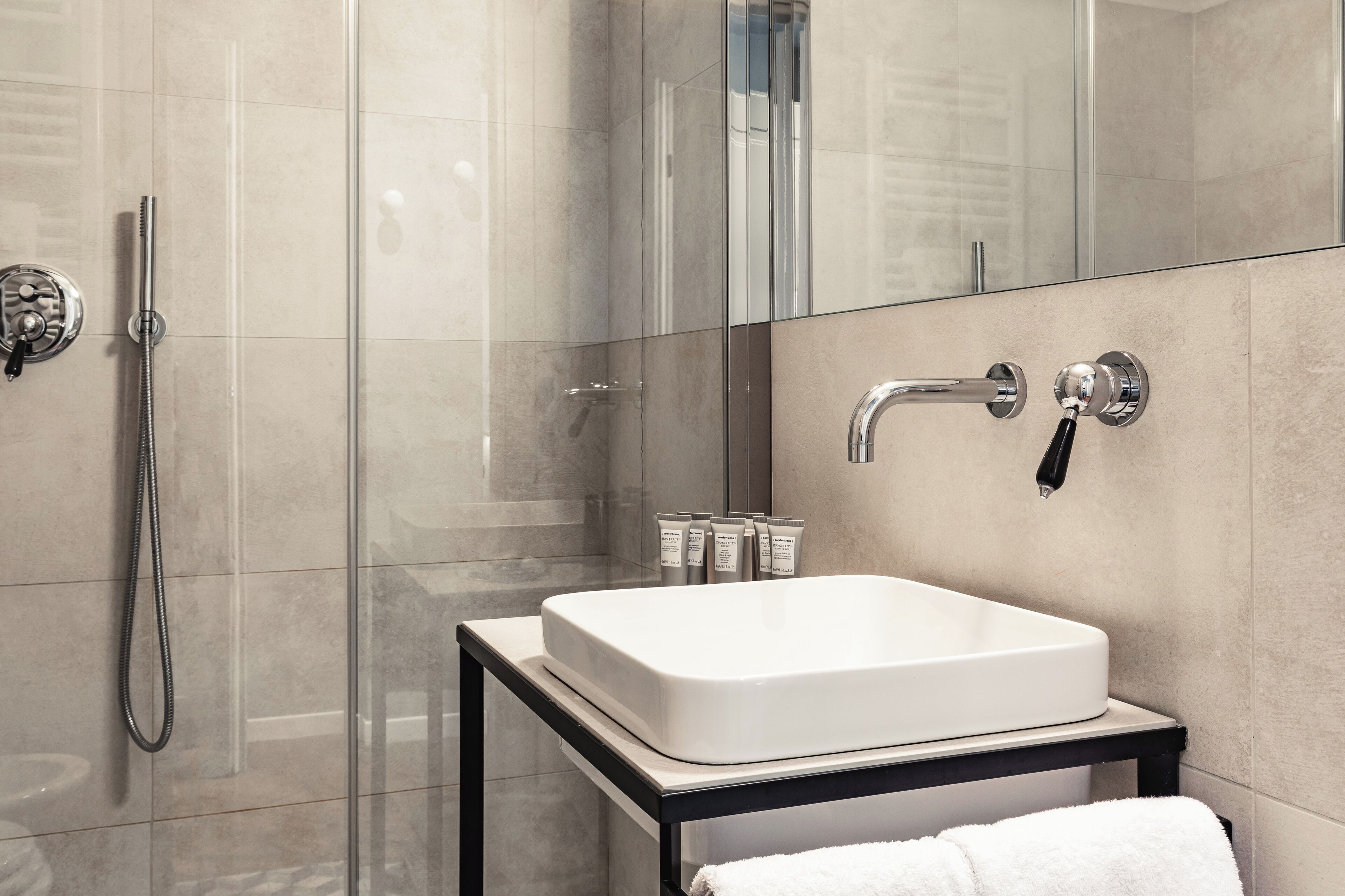 A modern bathroom with a glass shower enclosure, a white sink on a black countertop, and a towel on the floor.