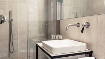A modern bathroom with a glass shower enclosure, a white sink on a black countertop, and a towel on the floor.